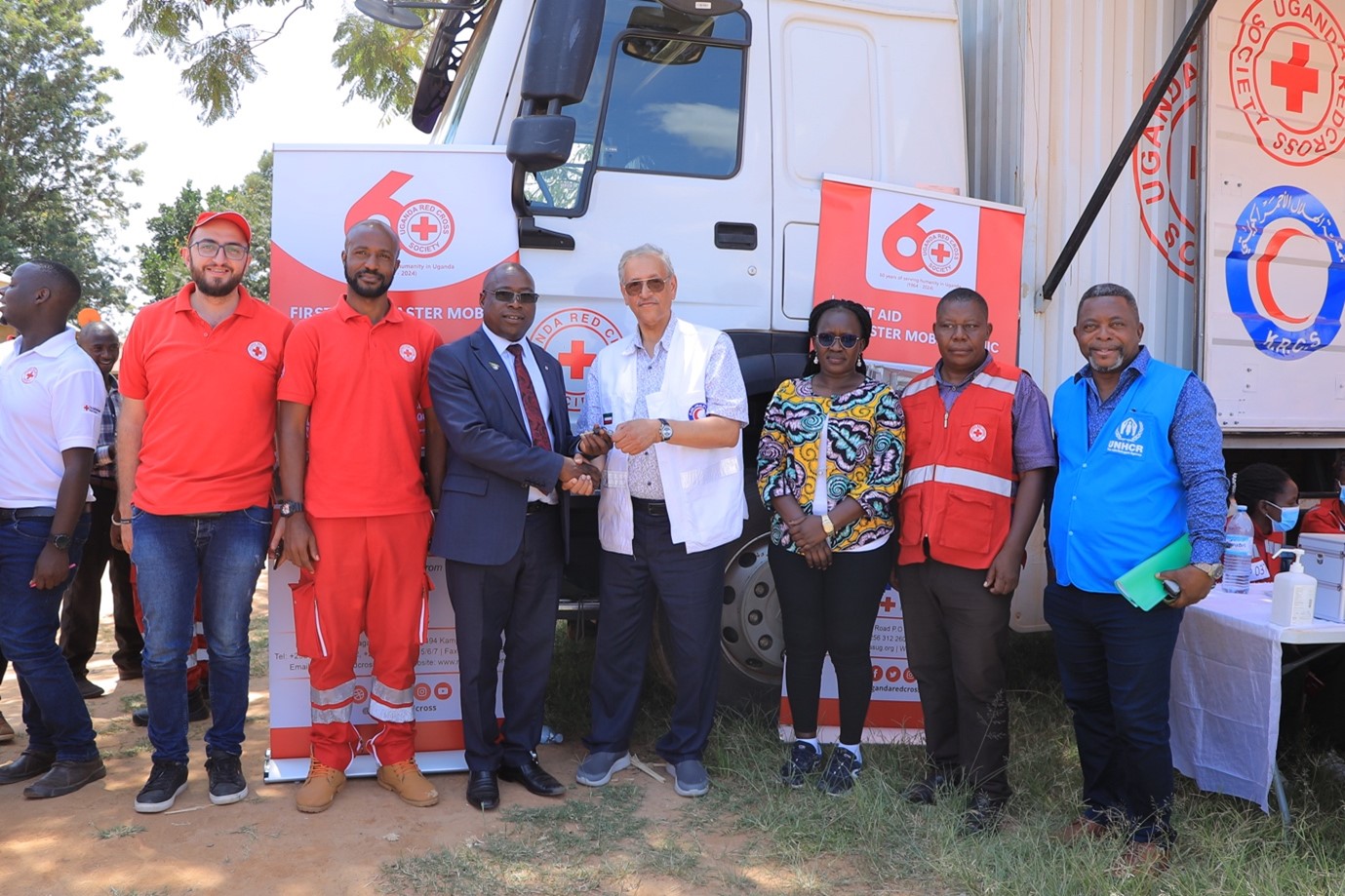 URCS Chairman Central Governing Board, Dr. Khalid Kirunda (centre in a suit) handing over receiving keys of the First Aid & Disaster Mobile Clinic from the Vice President of the Kuwait Red Crescent Society, Mr. Anwar Abdullah Al-Hassawi (Centre in a white Movement visibility jacket) at the commissioning event in Nakivale Refugee Settlement. 