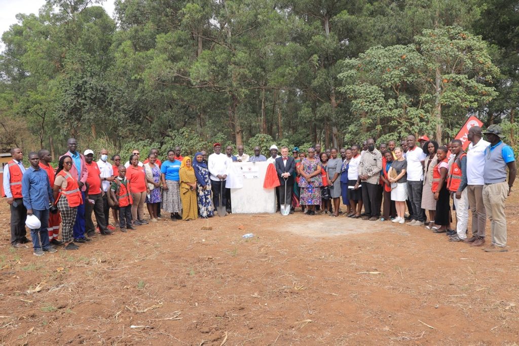 URCS secretary General, Robert Kwesiga (Left of the mark stone in a white shirt) possess for a group photo with Belgian Ambassador to Uganda, H.E. Chantry Hugues (right of the mark stone in a jacket) after the ground breaking ceremony of the women and youth center in Kyangwali refugee settlement. 