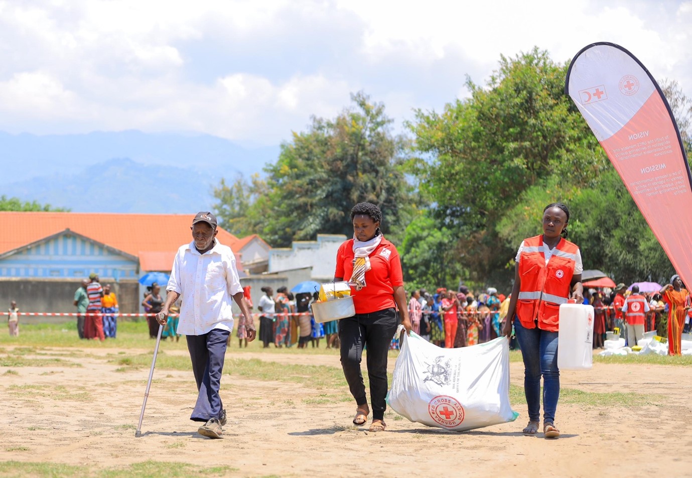 Uganda Red Cross Society volunteers assist Bwamite Thomas in carrying his relief items following the distribution exercise at Nyakasanga playground in Kasese District.